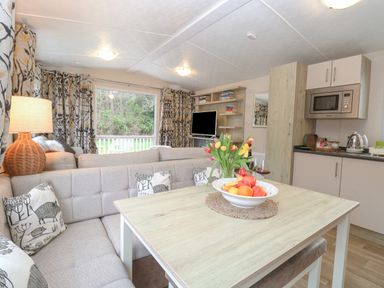 A living room with a beige sectional sofa a wooden dining table with fruit and flowers and a kitchen with cabinets and microwave at No 3 Foxburrow Hang in Belton