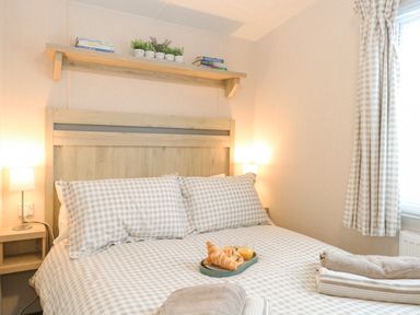 A bedroom with a bed with checkered bedding two lamps on wooden bedside tables and a shelf with small plants at No 3 Foxburrow Hang in Belton