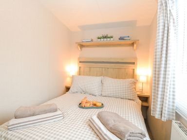 A bedroom with a double bed and checked bedding with towels and breakfast on the bed at No 3 Foxburrow Hang in Belton