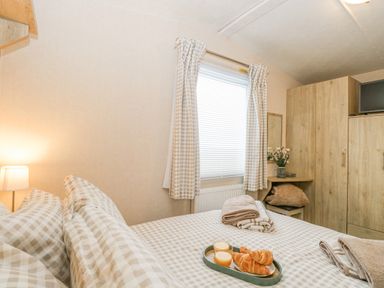 A bedroom with a bed covered in checked bedding and towels a window with checked curtains a wooden wardrobe and a small table with flowers at No 3 Foxburrow Hang in Belton
