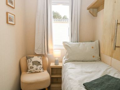 A small bedroom with a single bed a wooden nightstand with a lamp and a soft chair with a cushion at No 3 Foxburrow Hang in Belton