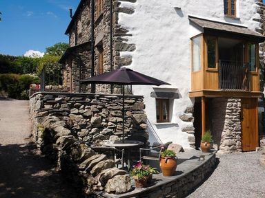 An outdoor seating area with a table umbrella and stone walls at The Cosy Peacock in Troutbeck