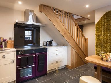 A kitchen with a purple oven and stove under wooden stairs at The Cosy Peacock in Troutbeck