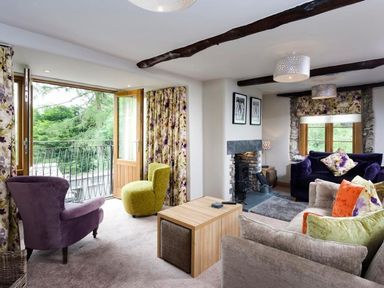 A living room with armchairs and sofas around a fireplace and a balcony door open at The Cosy Peacock in Troutbeck