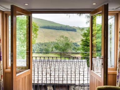 An open wooden double door leading to a small balcony with a metal railing overlooking green hills and trees at The Cosy Peacock in Troutbeck