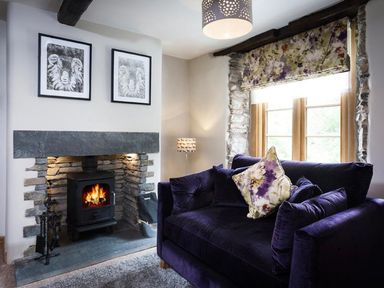 A living room with a fireplace and a dark purple sofa by a window at The Cosy Peacock in Troutbeck