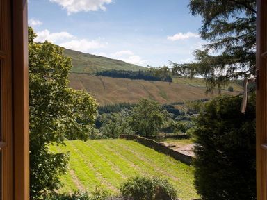 A view of a grassy field and hills through an open wooden window at The Cosy Peacock in Troutbeck