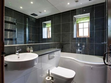 A bathroom with a white sink a toilet a bathtub with glass screen and two small windows at The Cosy Peacock in Troutbeck