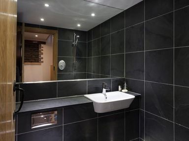 A bathroom with a wall-mounted sink and shower area with dark tiles at The Cosy Peacock in Troutbeck