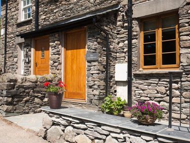 A stone exterior of a building with wooden doors and windows and potted flowers at The Cosy Peacock in Troutbeck