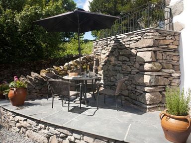 An outdoor stone patio with a round table and four chairs under a black umbrella at The Cosy Peacock in Troutbeck