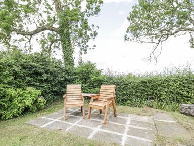 An outdoor space with wooden chairs on a stone patio at Woods Cottage near Raglan