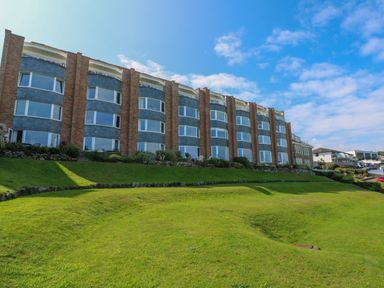 A row of multi-story buildings with large windows and a manicured lawn in front at Mariners Watch in Carbis Bay