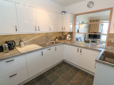 A kitchen with white cabinets a sink countertop appliances and a pass-through window to a living room at Mariners Watch in Carbis Bay
