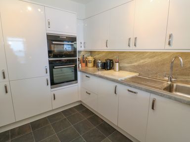 A kitchen with white cabinets a double oven a countertop with a kettle a French press a bread container a wine bottle a sink and tiled floor at Mariners Watch in Carbis Bay