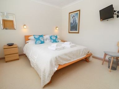A bedroom with a double bed two blue pillows two rolled towels a wooden nightstand and a wall-mounted TV at Mariners Watch in Carbis Bay