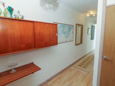 A hallway with wooden wall cabinets a mirror framed map and a rug on the floor at Mariners Watch in Carbis Bay