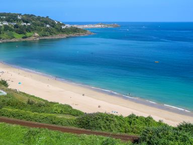 A sandy beach with people near the water and houses on a hill at Mariners Watch in Carbis Bay