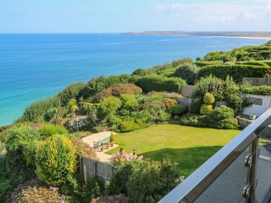 A garden with a lawn bench and various plants overlooking the sea at Mariners Watch in Carbis Bay