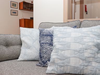 A grey sofa with three cushions featuring coral and fish patterns and a cabinet with glassware in the background at Mariners Watch in Carbis Bay
