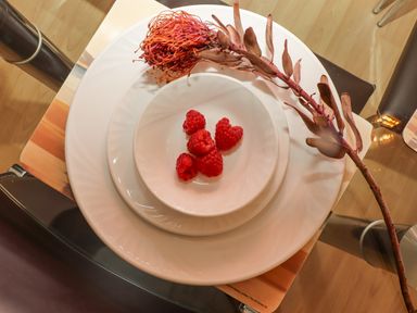 A glass table with stacked white plates a bowl with raspberries and a dried flower at Mariners Watch in Carbis Bay