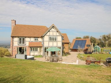 A large two storey house with a patio garden table umbrella and solar panels on a separate building at Cuckoo Pen Cottage Eastham near Tenbury Wells