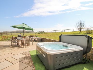 An outdoor patio area with a hot tub wooden table with umbrella chairs and garden seating at Cuckoo Pen Cottage in Eastham near Tenbury Wells