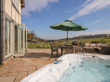 An outdoor patio with a hot tub table with chairs umbrella a barbecue and seating at Cuckoo Pen Cottage in Eastham near Tenbury Wells
