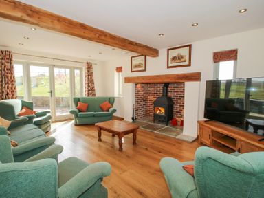 A living room with green sofas a wooden coffee table a wood stove fireplace and a large television at Cuckoo Pen Cottage Eastham near Tenbury Wells