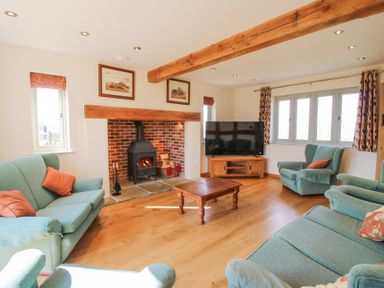 A living room with a wood burning stove fireplace green sofas a wooden coffee table and a television at Cuckoo Pen Cottage Eastham near Tenbury Wells