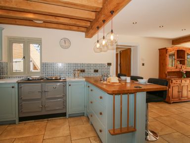 A kitchen with blue cabinets a wooden countertop a stove a tile backsplash and a wooden cabinet at Cuckoo Pen Cottage Eastham near Tenbury Wells