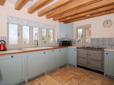 A kitchen with blue cabinets wooden countertops a grey stove and tiled floor at Cuckoo Pen Cottage in Eastham near Tenbury Wells