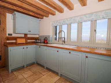 A kitchen with light blue cabinets wooden countertops a sink under windows and wooden beams on the ceiling at Cuckoo Pen Cottage in Eastham near Tenbury Wells
