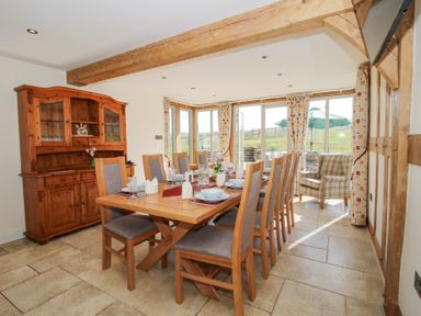 A dining room with a wooden table set for eight and a wooden cabinet at Cuckoo Pen Cottage in Eastham near Tenbury Wells