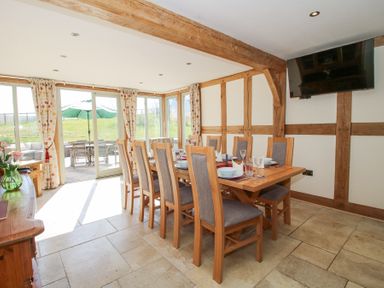 A dining room with a large wooden table and chairs near glass doors opening to a patio at Cuckoo Pen Cottage in Eastham near Tenbury Wells