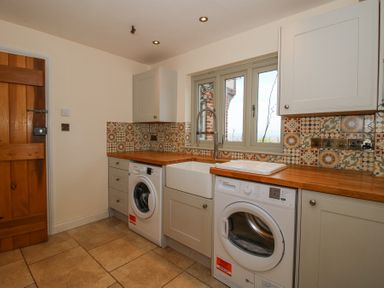 A laundry room with a wooden countertop washing machine dishwasher sink and patterned tile backsplash at Cuckoo Pen Cottage Eastham near Tenbury Wells