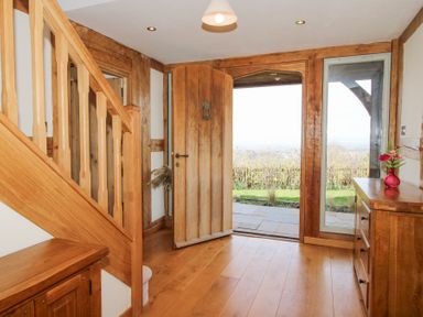 An entrance hall with a wooden staircase wooden furniture an open wooden front door and a glass panel at Cuckoo Pen Cottage Eastham near Tenbury Wells