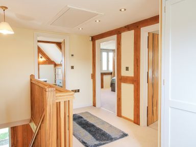 A hallway with wooden staircase railing doors leading to other rooms and a rug on the floor at Cuckoo Pen Cottage in Eastham near Tenbury Wells