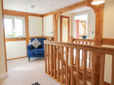 A hallway with wooden railings blue armchair and a window with a vase at Cuckoo Pen Cottage in Eastham near Tenbury Wells