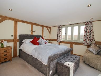 A bedroom with a double bed with pillows and a bench at the foot of the bed a sofa and a window with floral curtains at Cuckoo Pen Cottage Eastham near Tenbury Wells