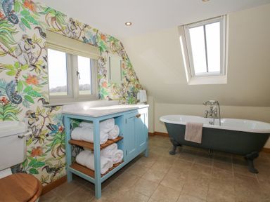 A bathroom with a clawfoot bathtub a wooden toilet seat a blue vanity with rolled towels and floral wallpaper at Cuckoo Pen Cottage Eastham near Tenbury Wells
