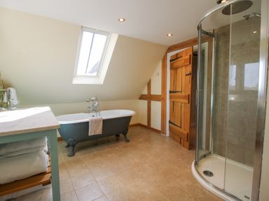 A bathroom with a clawfoot bathtub under a skylight a glass shower enclosure a wooden door and a counter with towels at Cuckoo Pen Cottage in Eastham near Tenbury Wells