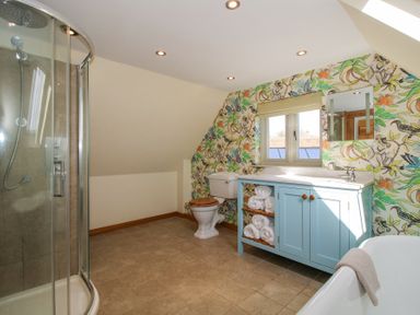 A bathroom with a curved glass shower cubicle a toilet with wooden seat a blue cabinet with rolled towels a sink and a bathtub with a towel at Cuckoo Pen Cottage Eastham near Tenbury Wells