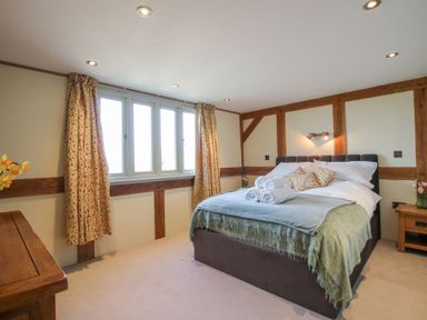 A bedroom with a bed with rolled towels and cushions beside wooden furniture at Cuckoo Pen Cottage in Eastham near Tenbury Wells