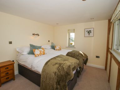 A bedroom with two beds pushed together covered in white bedding and green throws with a wooden side table and windows at Cuckoo Pen Cottage in Eastham near Tenbury Wells