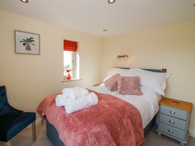 A bedroom with a bed with pink pillows and blanket bedside table and window with a red blind at Cuckoo Pen Cottage Eastham near Tenbury Wells