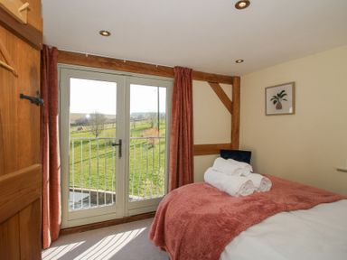 A bedroom with a bed covered by a red blanket and white towels near double glass doors showing a grassy outdoor area at Cuckoo Pen Cottage in Eastham near Tenbury Wells