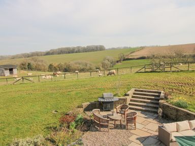 An outdoor patio area with chairs a table and a barbecue overlooking a fenced field with sheep at Cuckoo Pen Cottage in Eastham near Tenbury Wells