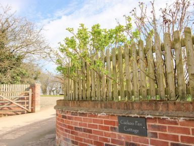 A wooden fence on a brick wall with a sign reading Cuckoo Pen Cottage and a wooden gate in the background at Eastham near Tenbury Wells