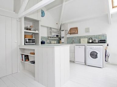 A white kitchen with appliances and shelves at The Net Loft in Mousehole